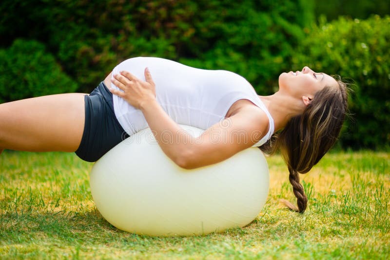Femmina incinta con la parte posteriore d'allungamento chiusa degli occhi sulla palla di yoga fotografia stock Femmina incinta con la parte posteriore d'allungamento chiusa degli occhi sulla palla di yoga fotografia stock