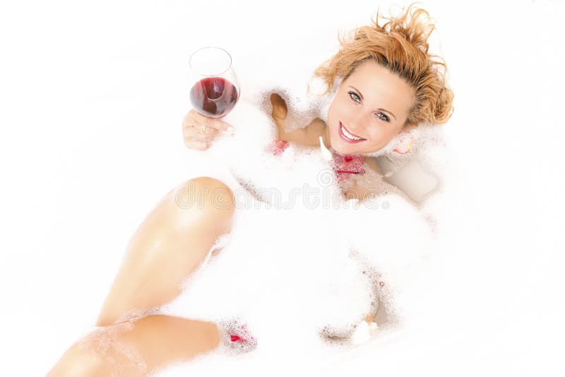 Femmina in vasca spumosa riempita di petali Tenuta del vetro di vino rosso immagini stock Femmina in vasca spumosa riempita di petali Tenuta del vetro di vino rosso immagini stock