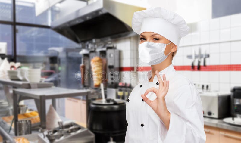 Femminile chef mascherato mostra un cartello ok in cucina