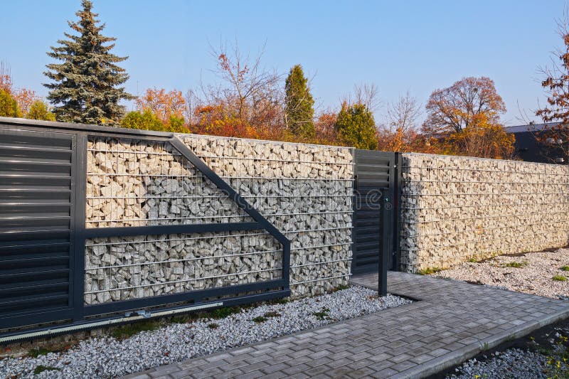 A fence made of gabions. Automatic entrance gate and wicket integrated into the wall made of a gabion