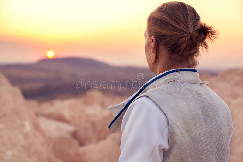 Fencer man on the rocky background and looking forward to the sun goes down stock photo Fencer man on the rocky background and looking forward to the sun goes down stock photo