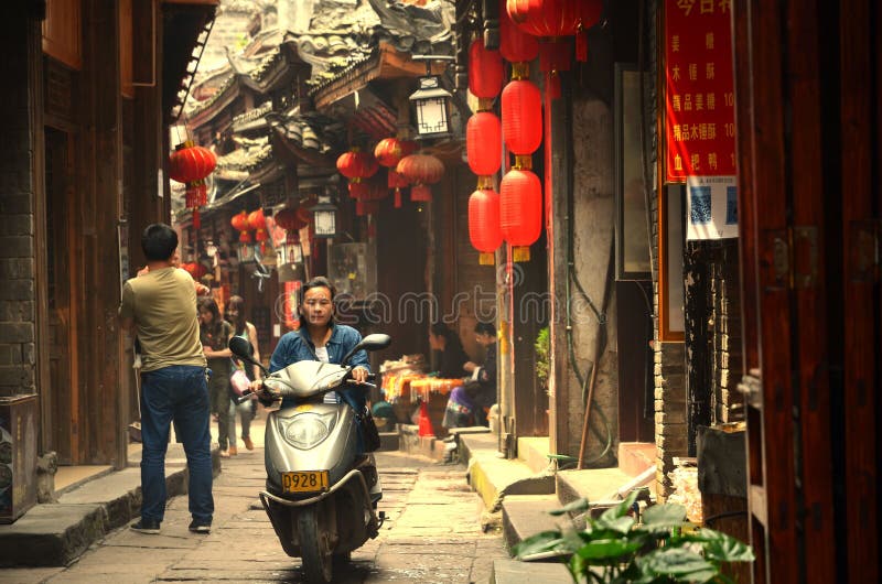 Fenghuang, China - 15 de maio de 2017: Mulher no velomotor na rua na cidade de Phoenix Fenghuang imagem de stock Fenghuang, China - 15 de maio de 2017: Mulher no velomotor na rua na cidade de Phoenix Fenghuang imagem de stock