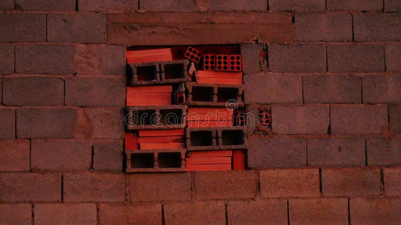Fenster mit Ziegeln in einem rustikalen spanischen oder ländlichen Gebäude. Im Herzen eines ländlichen spanischen Gebäudes ist nun ein Fenster, das einen Blick in das Innere bietet, abgesperrt. Der Rahmen, der ursprünglich Teil einer einfachen Struktur aus Betonblöcken war, wurde mit Steinen verschlossen, wodurch das Gebäude ein verwittertes und rustikales Aussehen erhält. Die Ziegel sind funktionell und verleihen dem Gebäude einen gewissen Charme und eine geschichtliche Note. Diese typische Landschaftsarchitektur, die durch ihre Praktikabilität gekennzeichnet ist, ruft in der spanischen Landschaft Zeitlosigkeit hervor.