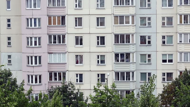 Fenêtres d'un bâtiment à panneaux de plusieurs étages. au fond du cadre, les cimes des arbres se balancent dans le vent clips vidéos