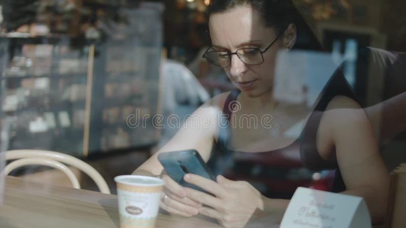 Fermer le téléphone cellulaire d'une femme. regarder la vidéo sur téléphone portable pendant la pause café. vue de l'extérieur. banque de vidéos