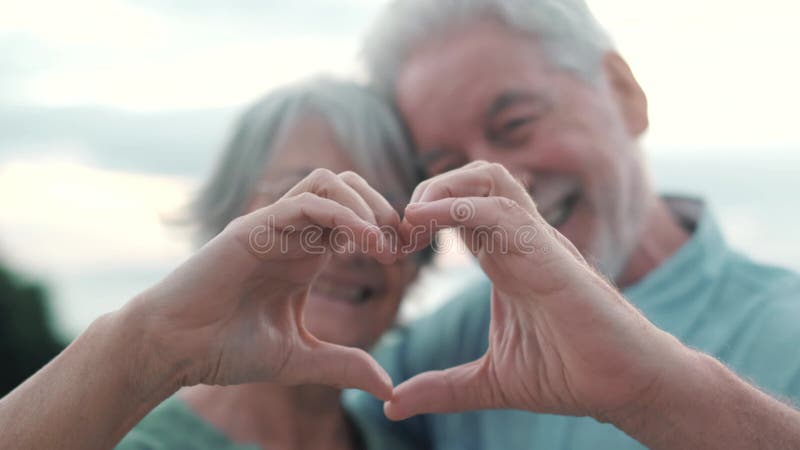Fermer portrait heureux sincère moyen-âge âgé retraité couple faisant un geste de coeur avec des doigts montrant l'amour ou clips vidéos