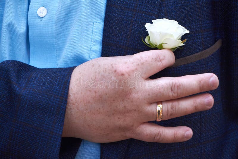 Close up of a white rose buttonhole in a pocket of a blue suit jacket, selective focus. Close up of a white rose buttonhole in a pocket of a blue suit jacket, selective focus