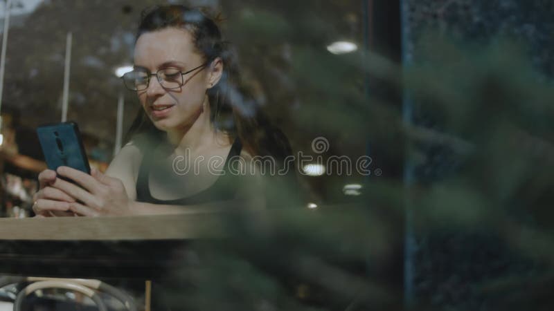 Fermeture d'une femme tenant le téléphone cellulaire dans un caffe. prendre un selfie sur un téléphone portable pendant une pause clips vidéos
