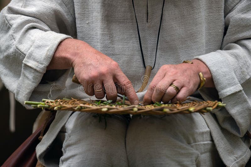 Fermez-vous de l'artisan portant les vêtements ruraux faisant le panier en osier des brindilles Technique de tissage faite main t photographie stock Fermez-vous de l'artisan portant les vêtements ruraux faisant le panier en osier des brindilles Technique de tissage faite main t photographie stock