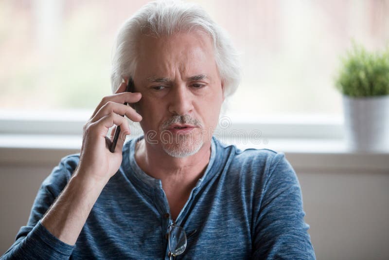 Fermez-vous de l'homme âgé sérieux ayant l'entretien de téléphone photographie stock Fermez-vous de l'homme âgé sérieux ayant l'entretien de téléphone photographie stock