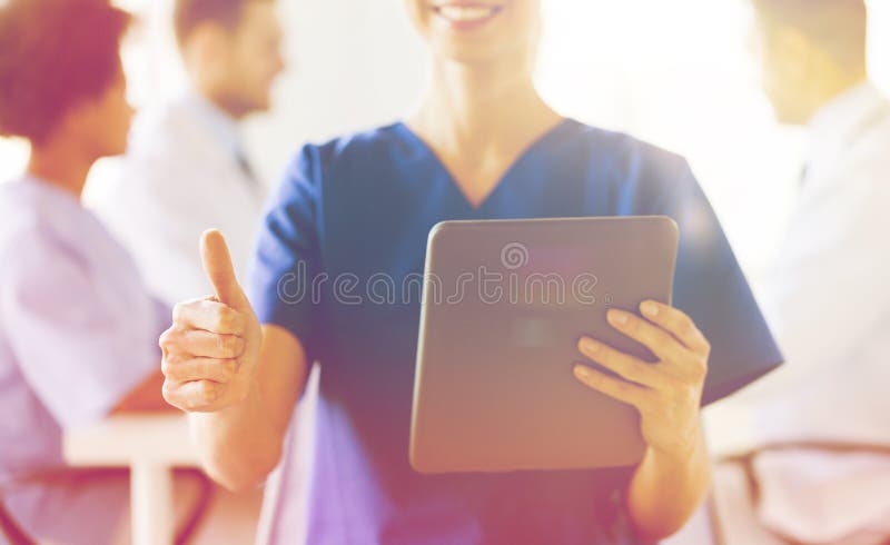 Fermez-vous de l'infirmière avec le PC de comprimé montrant des pouces photo stock