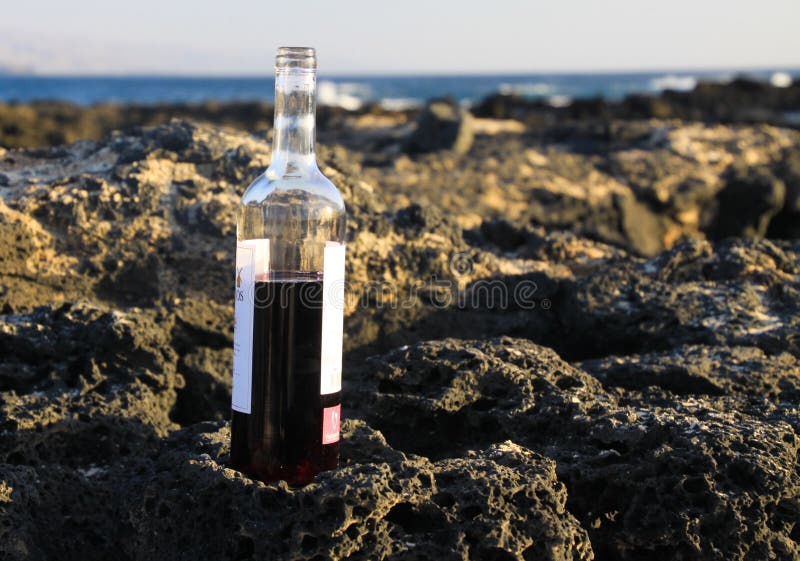 Fermez-vous de la bouteille à moitié pleine de vin rouge sur des roches de plage avec le fond de ressacs - EL Cotillo, Fuertevent photo libre de droits Fermez-vous de la bouteille à moitié pleine de vin rouge sur des roches de plage avec le fond de ressacs - EL Cotillo, Fuertevent photo libre de droits