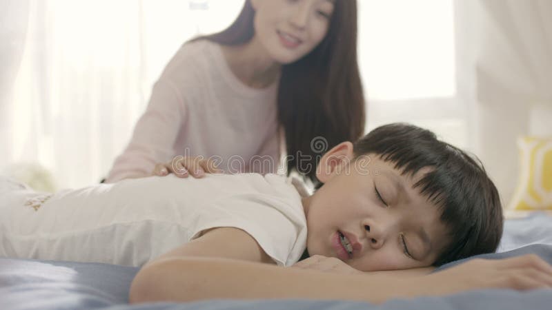 Fermez-vous de la jeune mère asiatique souriant et réveillant son fils dans le matin