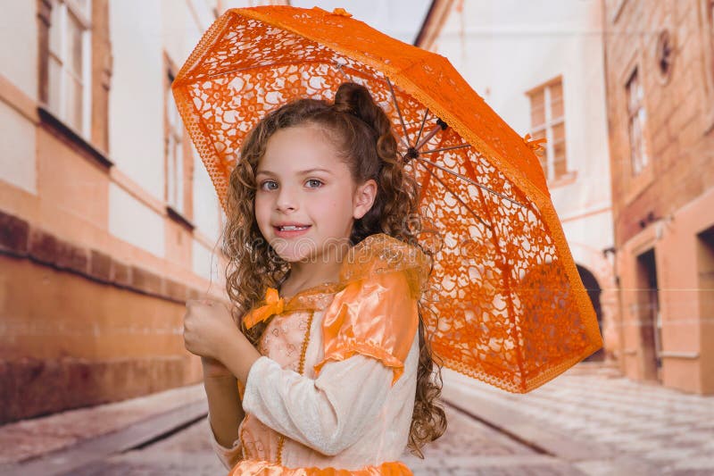 Fermez-vous de la petite belle fille utilisant un beau costume colonial et jugeant un parapluie orange dans brouillé image libre de droits Fermez-vous de la petite belle fille utilisant un beau costume colonial et jugeant un parapluie orange dans brouillé image libre de droits