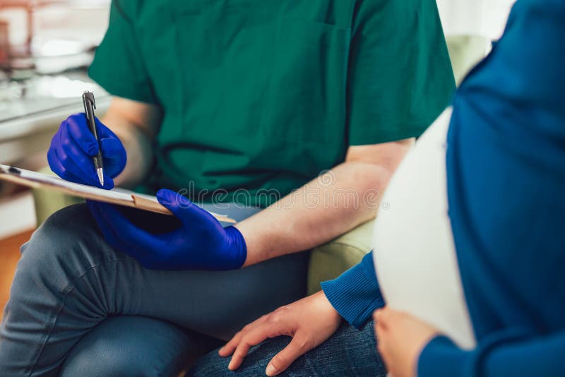 Fermez-vous du docteur masculin tenant le document tout en se reposant avec la femme enceinte image libre de droits Fermez-vous du docteur masculin tenant le document tout en se reposant avec la femme enceinte image libre de droits
