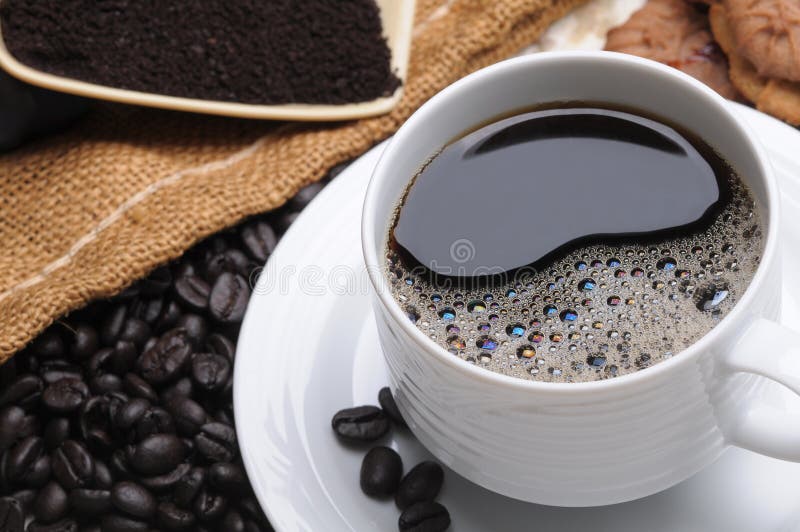 Close up of a delicious fresh hot cup of coffee with with beans grinds and cookies shallow DOF horizontal format. Close up of a delicious fresh hot cup of coffee with with beans grinds and cookies shallow DOF horizontal format