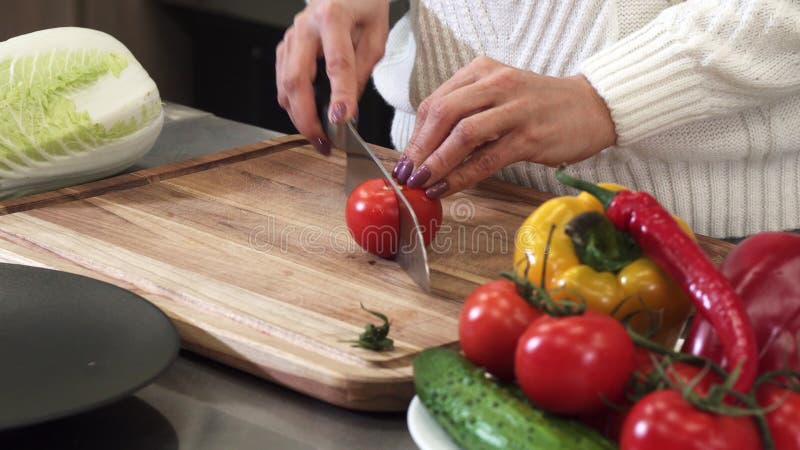 Fermez-vous vers le haut du tir cultivé d'une femme coupant en tranches la tomate sur une planche à découper en bois images stock Fermez-vous vers le haut du tir cultivé d'une femme coupant en tranches la tomate sur une planche à découper en bois images stock