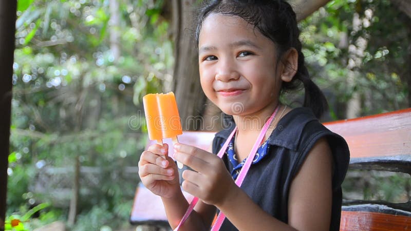 Fermez-vous vers le haut du tir de la petite fille heureuse mignonne de l'Asie tenant la crème glacée orange banque de vidéos
