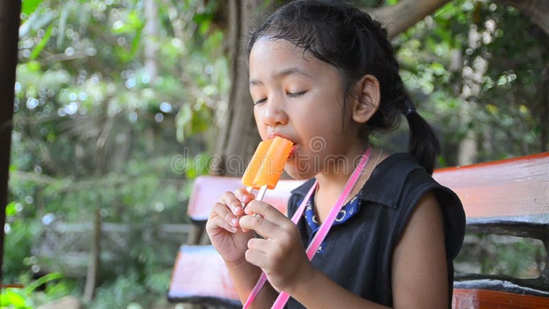 Fermez-vous vers le haut du tir de la petite fille heureuse mignonne de l'Asie tenant la crème glacée orange banque de vidéos