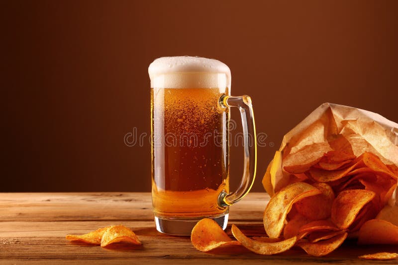 Fermez-vous vers le haut du verre de bière et des pommes chips au-dessus du brun photos libres de droits Fermez-vous vers le haut du verre de bière et des pommes chips au-dessus du brun photos libres de droits