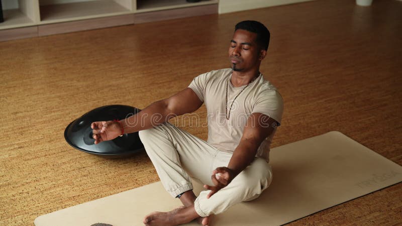 Fernsicht auf den ruhigen afrikanischen Mann, der auf Yogamattel sitzt, mit geschlossenen Augen, die allein auf dem Boden meditier stock footage