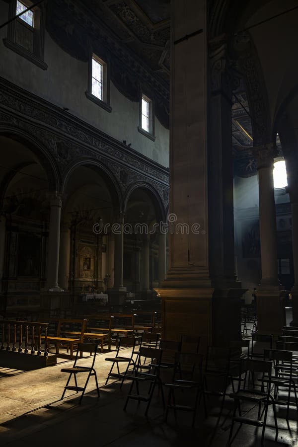 June 4, 2023 - Ferrara. The dark and silent interior of an ancient church, with light filtering through the rose window, illuminating the chairs and benches in the central nave. June 4, 2023 - Ferrara. The dark and silent interior of an ancient church, with light filtering through the rose window, illuminating the chairs and benches in the central nave