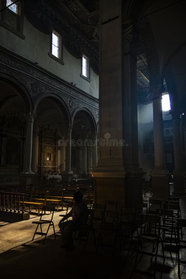 June 4, 2023 - Ferrara. The dark and silent interior of an ancient church. Light filtering through the rose window, illuminating the chairs and benches. A solitary believer is absorbed in prayer. June 4, 2023 - Ferrara. The dark and silent interior of an ancient church. Light filtering through the rose window, illuminating the chairs and benches. A solitary believer is absorbed in prayer