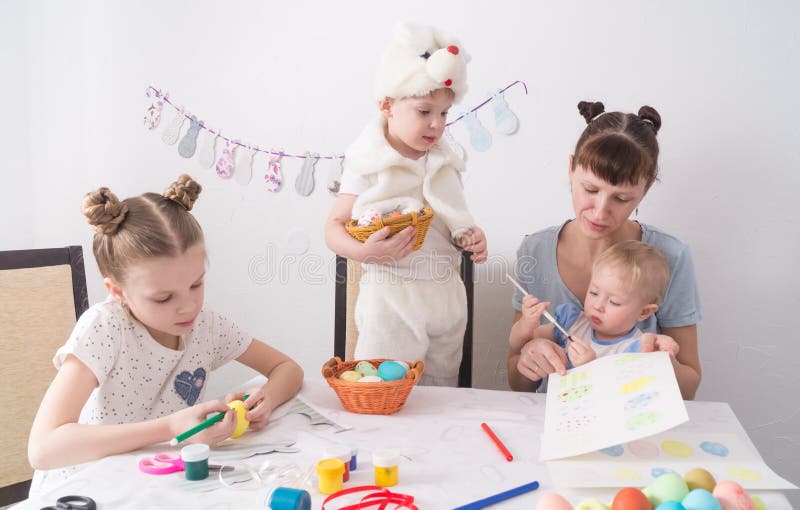 Festival de Pascua: La familia en la tabla La mamá muestra a niños cómo pintar los huevos de Pascua imagen de archivo Festival de Pascua: La familia en la tabla La mamá muestra a niños cómo pintar los huevos de Pascua imagen de archivo