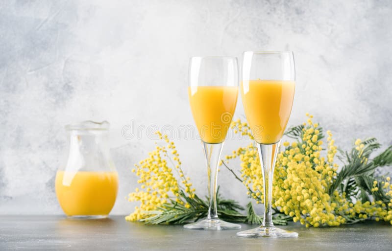 Festive alcohol cocktail mimosa with orange juice and cold dry champagne or sparkling wine in glasses, gray bar counter background with flowers, place for text, selective focus