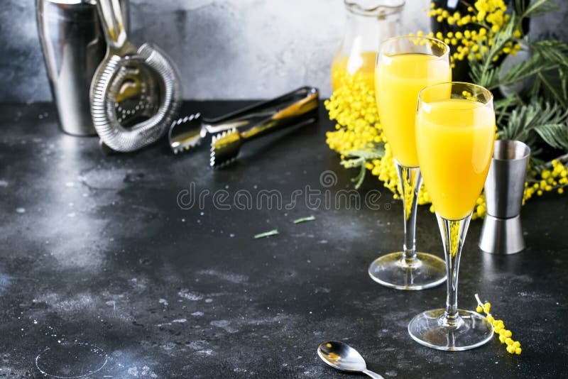 Festive alcohol cocktail mimosa with orange juice and cold dry champagne or sparkling wine in glasses, gray bar counter background with flowers, place for text, selective focus