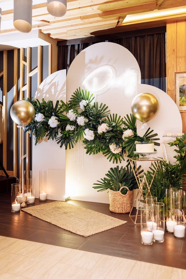 festive arch with white cake with berries, gold air balloons, white flowers, candles, monstera leaves on birthday party