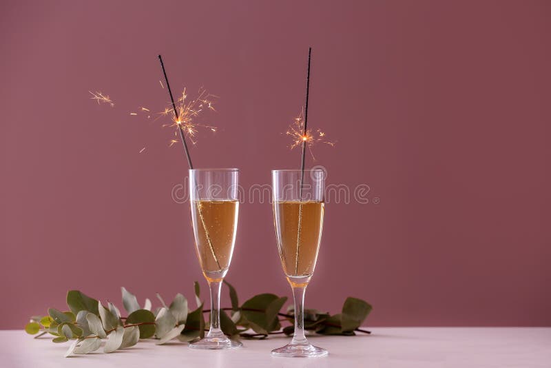 Festive Christmas sparklers in glasses with champagne on table against color background stock images Festive Christmas sparklers in glasses with champagne on table against color background stock images