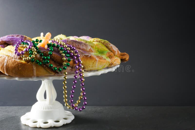 Festive gold, green, and purple King Cake for Mardi Gras with traditional beads and a baby figurine; copy space