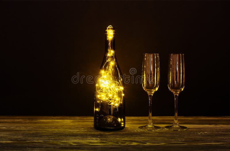 Festive romantic postcard background. Shining champagne wineglasses, wooden table on black. Cozy still life composition. Bottle decorated garland. Christmas royalty free stock images Festive romantic postcard background. Shining champagne wineglasses, wooden table on black. Cozy still life composition. Bottle decorated garland. Christmas royalty free stock images
