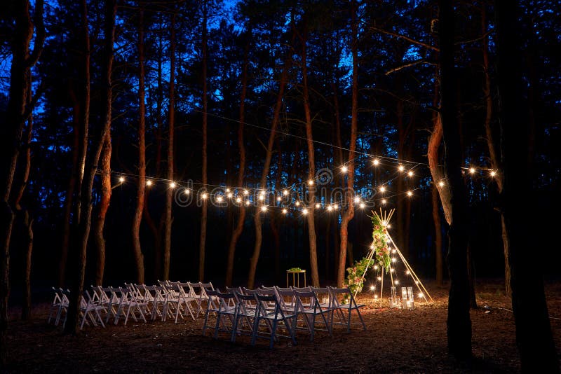 Festive string lichting op boho tipi boogdecor op buitenste trouwceremonie in dennenbos bij nacht