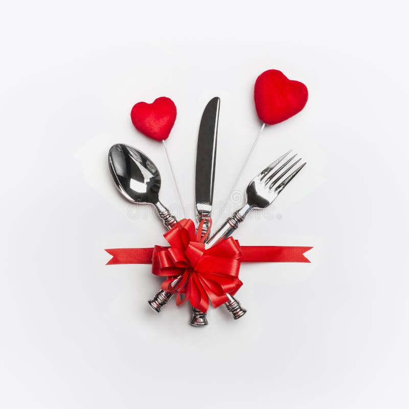 Festive table place setting with cutlery and red bow and two hearts on white background. Layout for Valentines day dinner