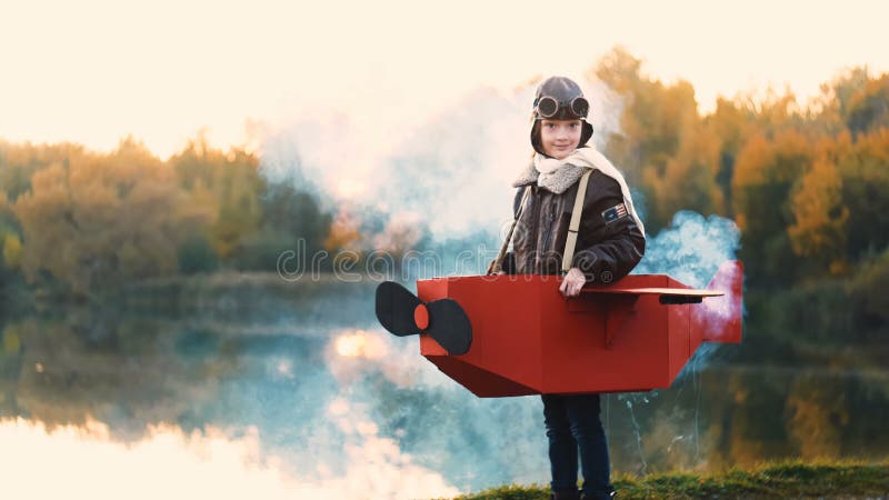 Fetiță aviatoare fericită care stă la Sunset Lake în avion de carton îmbrăcat cu fum colorat care joacă rolul de pilot lent. stock video