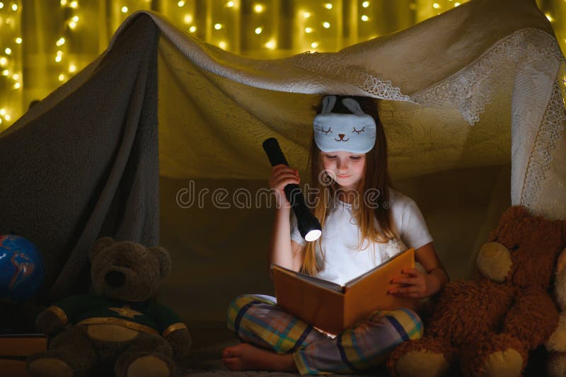 Fetiță fericită râzând și citind cărți în întuneric într-un cort acasă royalty free stock image
