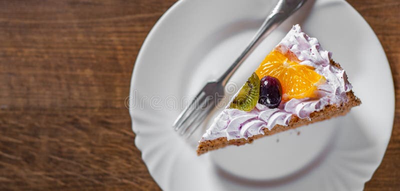 Fetta di torta di compleanno stratificata con crema con frutta in un piatto su di legno fotografie stock libere da diritti Fetta di torta di compleanno stratificata con crema con frutta in un piatto su di legno fotografie stock libere da diritti