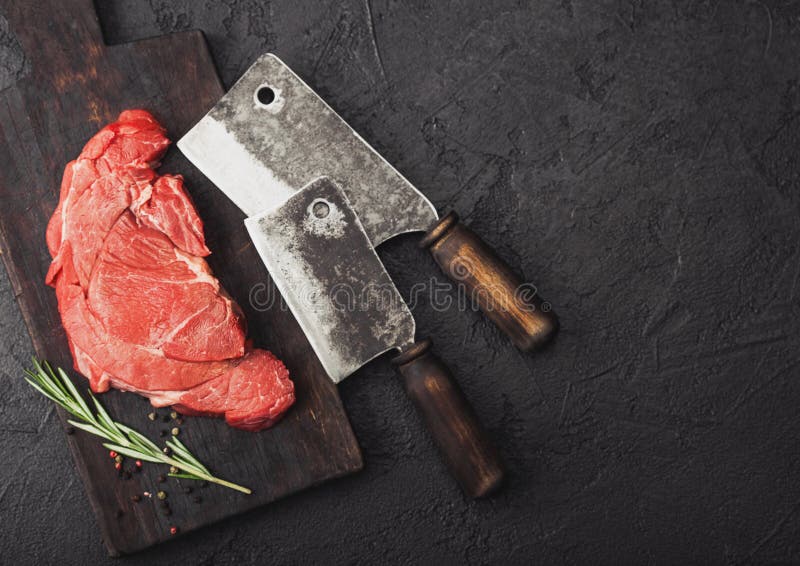 Fetta organica cruda fresca di raccordo di brasatura della bistecca sul tagliere con gli scuri della carne su fondo di pietra ner fotografia stock libera da diritti Fetta organica cruda fresca di raccordo di brasatura della bistecca sul tagliere con gli scuri della carne su fondo di pietra ner fotografia stock libera da diritti