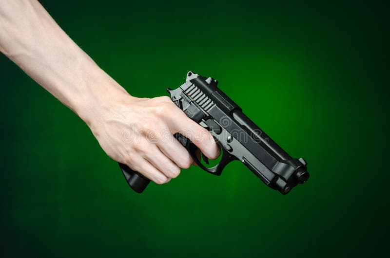 Feuerwaffen und Mörderthema: menschliche Hand, die ein Gewehr auf einem dunkelgrünen Hintergrund lokalisiert im Studio hält