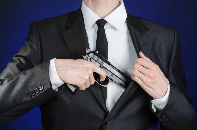 Feuerwaffen und Sicherheitsthema: ein Mann in einem schwarzen Anzug, der ein Gewehr auf einem dunkelblauen Hintergrund im Studio
