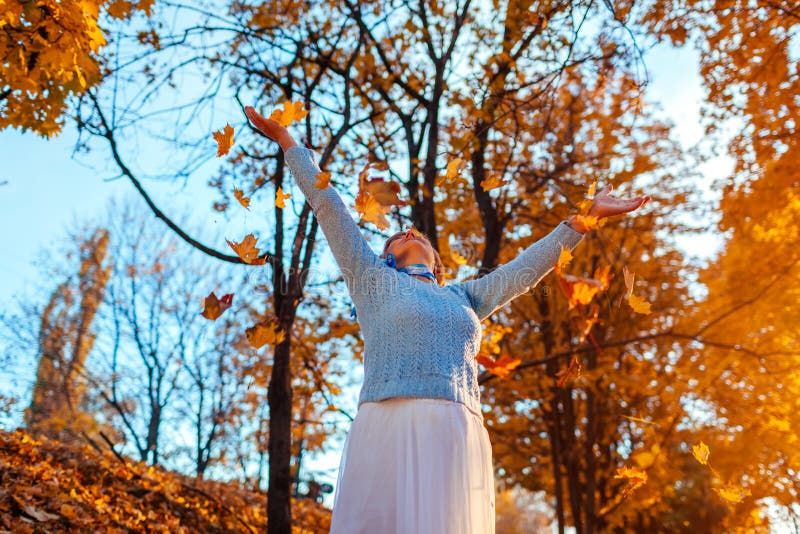 Feuilles de lancement de femme d'une cinquantaine d'ann?es dans la femme sup?rieure de for?t d'automne ayant l'amusement dehors image stock Feuilles de lancement de femme d'une cinquantaine d'ann?es dans la femme sup?rieure de for?t d'automne ayant l'amusement dehors image stock