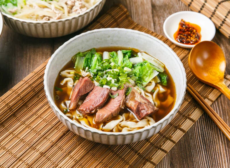 Fideos clásicos de ternera tendon con salsa de chile cebolla de primavera cuchara de madera y palillos servidos en plato aislado e foto de archivo