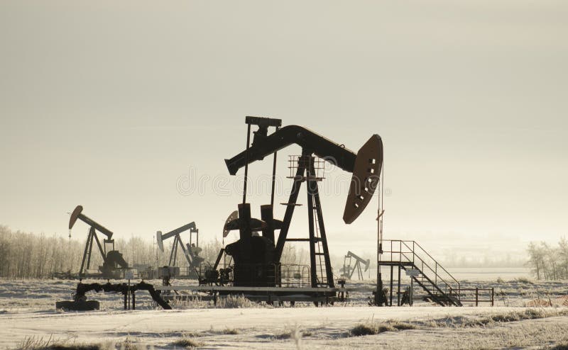 Field with oil pump jacks surrounded by greenery under sunlight stock photography Field with oil pump jacks surrounded by greenery under sunlight stock photography
