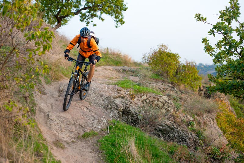Fietser in Sinaasappel die de Bergfiets berijden op Autumn Rocky Trail Extreme Sport en het Concept van Enduro Biking royalty-vrije stock foto Fietser in Sinaasappel die de Bergfiets berijden op Autumn Rocky Trail Extreme Sport en het Concept van Enduro Biking royalty-vrije stock foto
