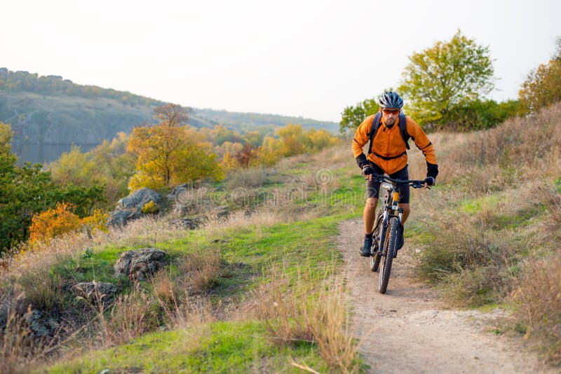 Fietser in Sinaasappel die de Bergfiets berijden op Autumn Rocky Trail Extreme Sport en het Concept van Enduro Biking stock afbeeldingen Fietser in Sinaasappel die de Bergfiets berijden op Autumn Rocky Trail Extreme Sport en het Concept van Enduro Biking stock afbeeldingen