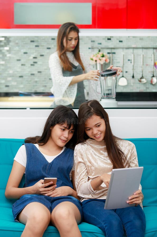 Figlia che esamina la madre bianca dello smartphone che cucina nella cucina fotografia stock libera da diritti Figlia che esamina la madre bianca dello smartphone che cucina nella cucina fotografia stock libera da diritti
