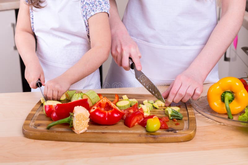 Figlia d'istruzione della madre per tagliare le verdure fotografia stock Figlia d'istruzione della madre per tagliare le verdure fotografia stock