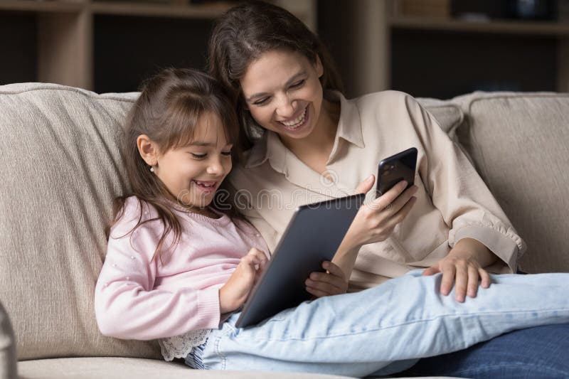 Figlia single sorridente che usa dispositivi digitali sul divano fotografie stock libere da diritti